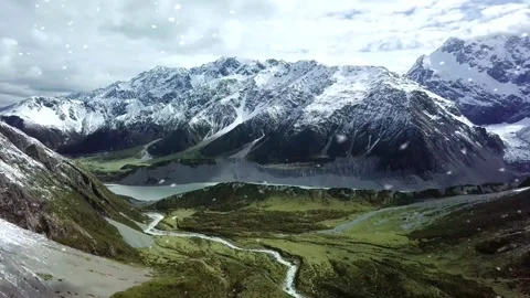 Snowfall Begins Over Snow-Capped Mountain and Green Valley Stock Footage 325329141
