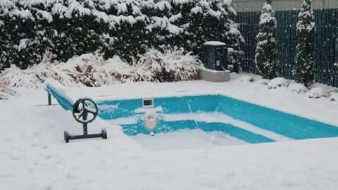 Snowfall covers backyard swimming pool with safety cover rolled up. Vídeos de archivo 334924113