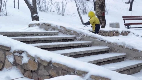 Snowfall in winter park, boy in yellow suit and masonry stairs in snow season 스톡 동영상 159057812