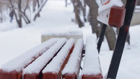 Snowfall in winter park, empty snowy bench under snow with snowdrifts by walkway Video stock 159057875