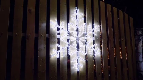 A snowflake made from Christmas lights hanging on the wooden fence. HD Video stock 83673381