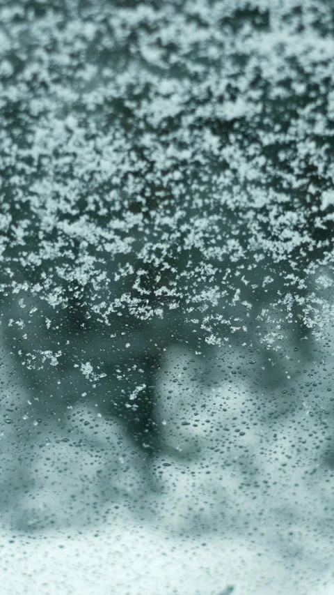 Snowflakes fall on the windshield of a car on a snowy winter day. Snowy weather. Video stock 329923518