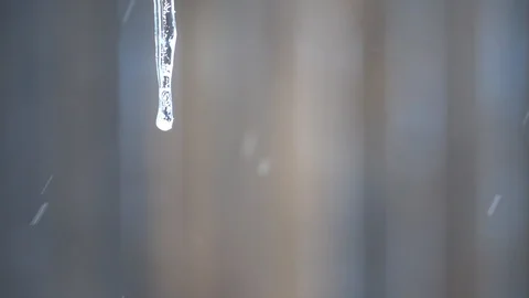 Snowflakes falling behind a single icicle over a brown background in the wint Stock Footage 102675791