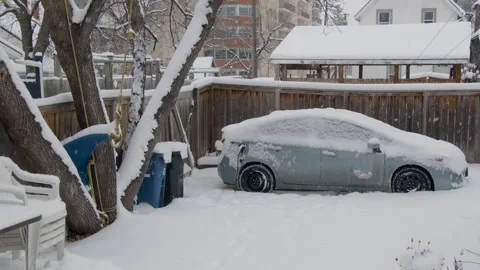 Snowing backyard with parked electric car, recycling bins, tree, fence Stock Footage 295919747