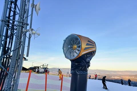 Snowmaking machine on ski slope with clear blue sky and people skiing Stock Photos