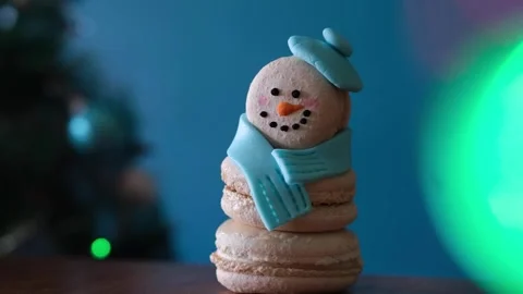 Snowman dessert macaron decorated with hat and scarf against Christmas tree Stock-Footage 255922435