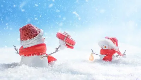 Snowman hands out a gift to the second snowman with a flashlight Stock Photos