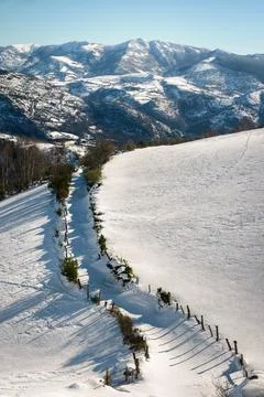 Snowy landscape with a path between fields and mountains in the background Stock Photos