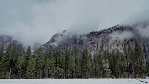 Snowy meadow below cloud covered granite cliffs Video stock 347988472