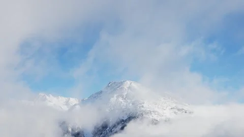 Snowy mountain with clouds and mist surrounding it and blue sky in background Stock Footage 319065910