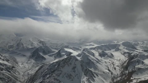 Snowy mountain landscape with dramatic clouds, camera pans across scene Видео 325024219