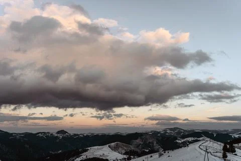 Snowy mountain landscape with dramatic clouds and soft evening light at sunse Stock Photos