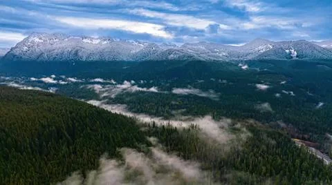 Snowy mountain range with forest and cloudy sky Stock Photos