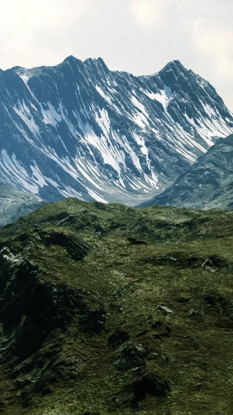 Snowy mountain range rises above grassy hills in the afternoon light Stockbeeldmateriaal 334050245