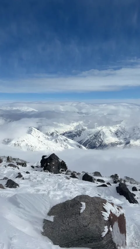 A snowy mountain summit overlooks distant ridges rising above clouds beneath blu Stock Footage 338001652