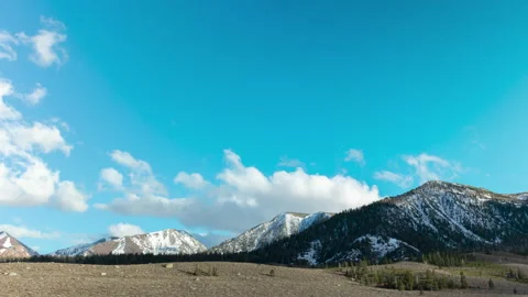 Snowy mountains with rolling clouds and blue sky 4k 24fps Stock Footage 132872944