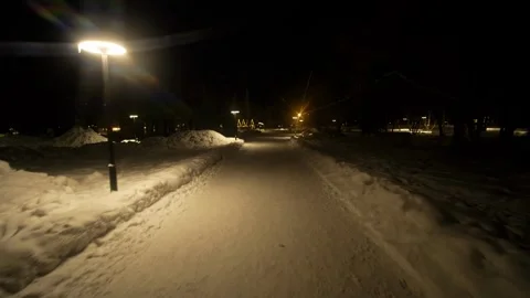 Snowy park paths at night, illuminated by warm yellow street lamps. Stock Footage 328418196
