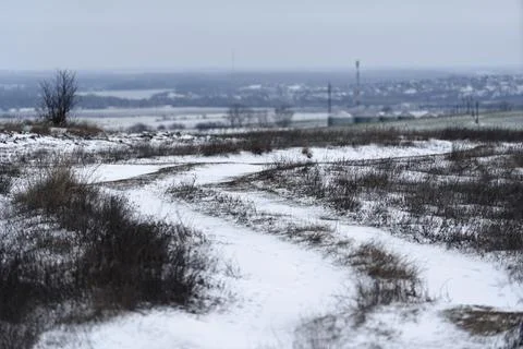 Snowy path winds through field on a cloudy winter day in an open landscape Foto stock