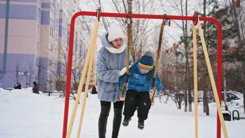 Snowy playground joy. Parent gently pushes child on frosty playground equipment Stock Footage 337726447