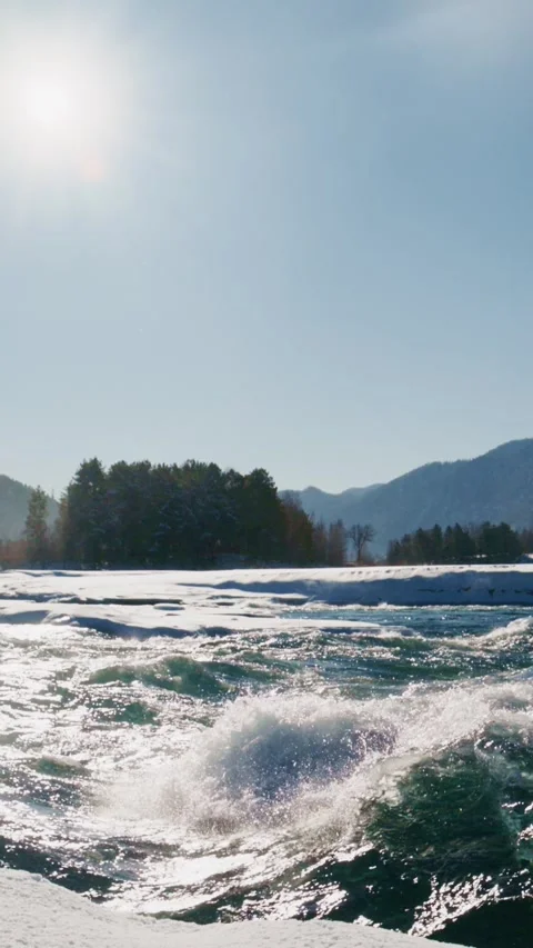 Snowy river scene with splashing waves and mountains in the background under Video stock 312861522
