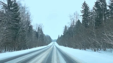 Snowy road driving through forest area in winter with cloudy sky and trees along Stock Footage 325808106