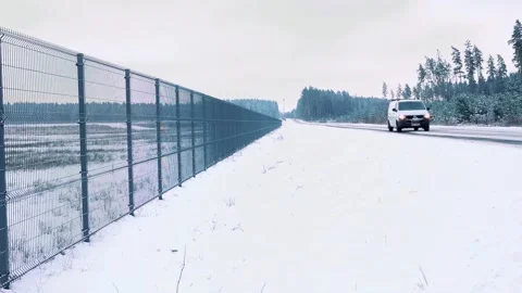 A snowy road runs parallel to a tall metal fence, stretching endlessly into the Stock Footage 328083171