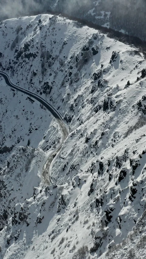 Snowy Road Winding Through Steep Mountain Pass in Winter Landscape Vídeos de archivo 334774579