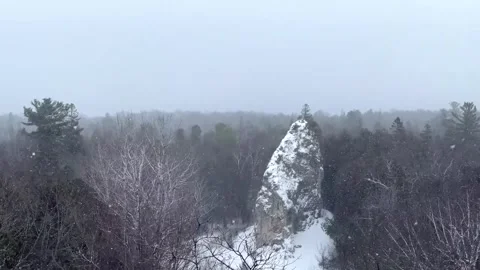 Snowy rock pinnacle with a lone tree in a winter forest under gentle snowfall Stock Footage 325477407