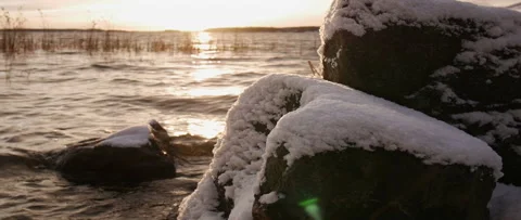 Snowy rocks with sun setting over waves Stock Footage 165683924