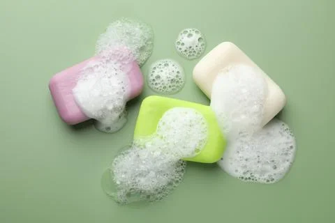 Soap bars with foam on green background, flat lay Stock Photos