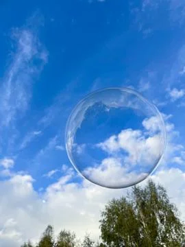 Soap bubble against the background of a cloudy blue sky. Stock Photos