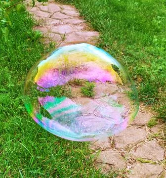 Soap bubble on the background of green grass and concrete path Foto stock