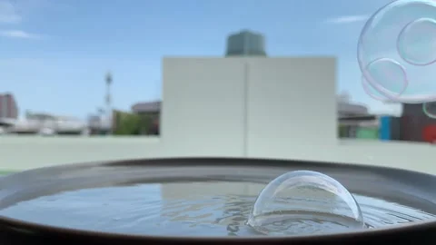 Soap bubbles bouncing passed, some dropped into shallow water on a flat dish. 스톡 동영상 130373576