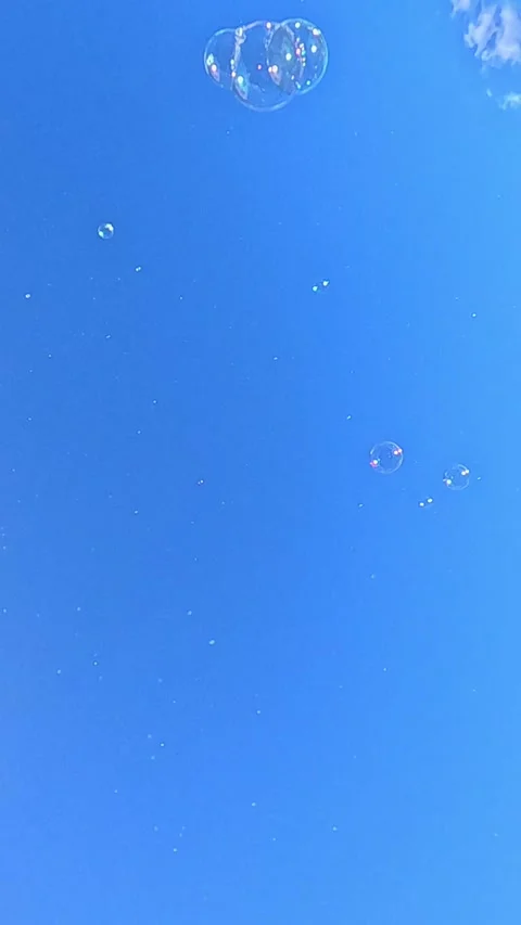 Soap bubbles drifting upward across clear blue sky background Stock Footage 324056731
