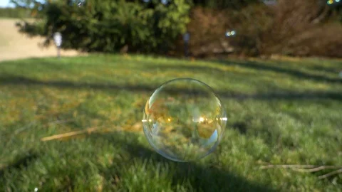 Soap bubbles floating along above the green lawn then popping as it Stock Footage 129677239