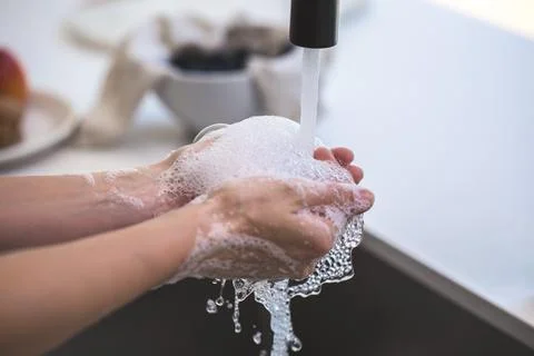 Soap bubbles gather in a pair of hands as they are washing in the kitchen. Stock Photos