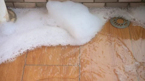 Soapy foam slowly draining through floor drain on wood patterned tile floor Stock Footage 346442953