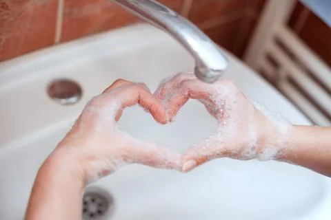 Soapy hand making heart shape in bathroom Stock Photos