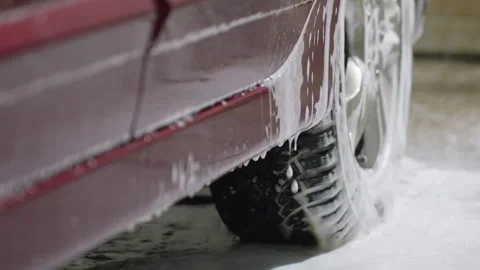 Soapy water dripping from red car body near tire during washing process Stock Footage 310177435