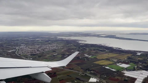 Soar over patchwork farmlands and shimmering coastal bays from airplane wing, 動画素材 337946054