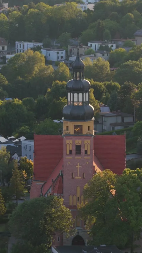 Soaring drone view flying towards historic church tower with red roof at sunset Vidéo 347883160