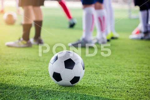 Soccer ball on green artificial turf with blurry soccer players standing Stock Photos