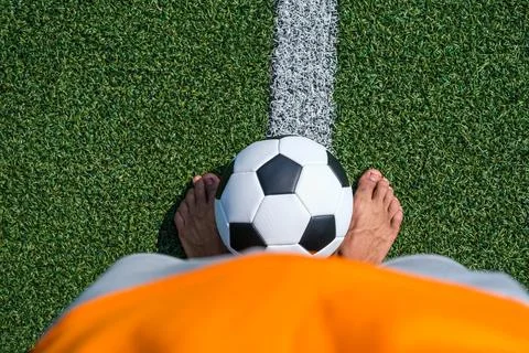 Soccer ball lying between bare feet of african american man on soccer field Stock Photos