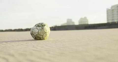 Soccer ball rests on sandy beach with city buildings in background Ilustración de archivo