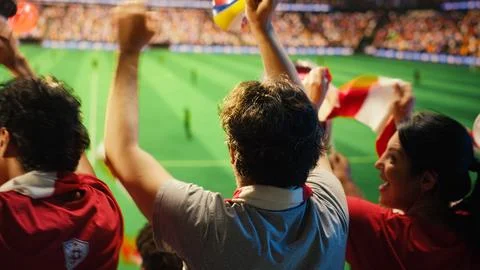 Soccer fans in red shirts react with excitement to goal scored during match Stock Photos