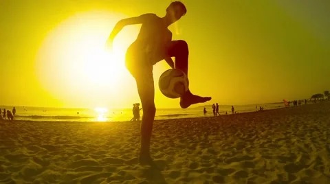 A soccer player is dribbling and doing tricks with the ball on beach sunset, Stock Footage