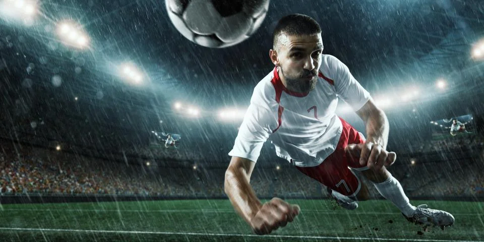 Soccer player performs an action play on a professional rainy stadium Stock Photos