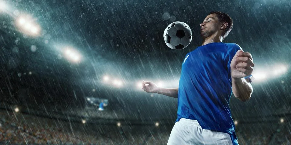 Soccer player performs an action play on a professional rainy stadium Stock Photos