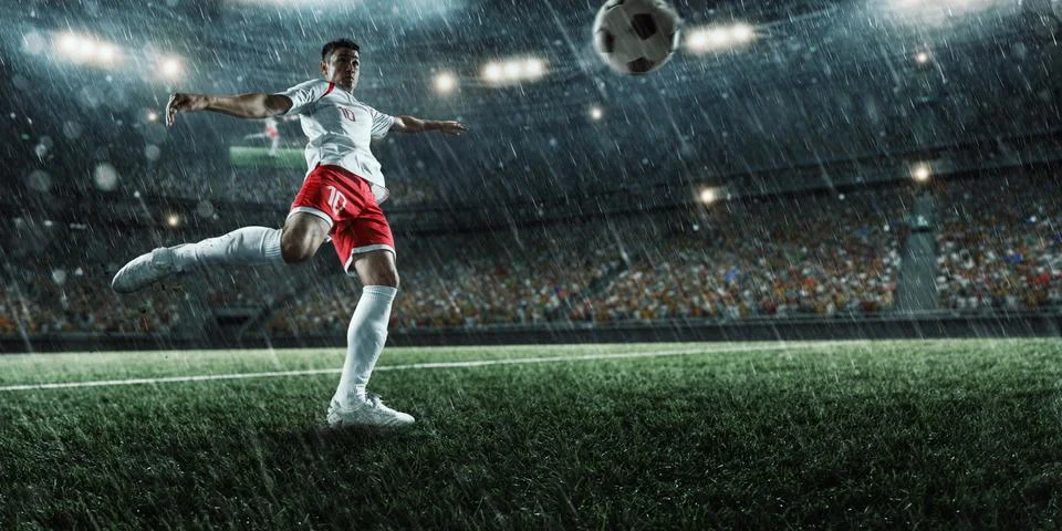 Soccer player performs an action play on a professional rainy stadium Stock Photos