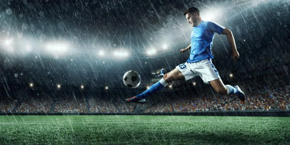 Soccer player performs an action play on a professional rainy stadium Stock Photos